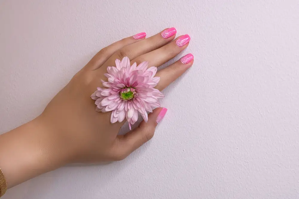 Mano con esmaltado en gel rosa sosteniendo una flor